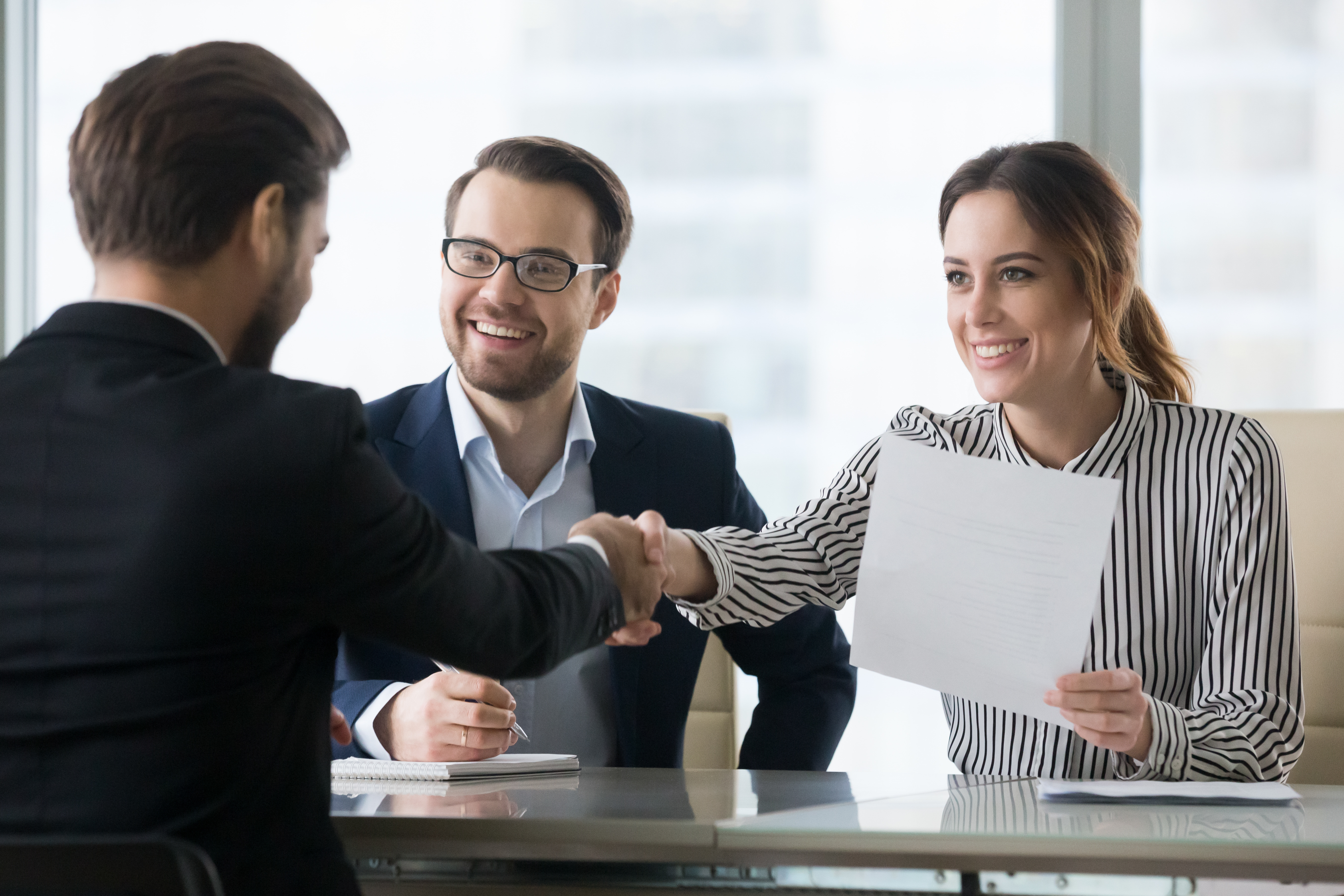 Smiling employers handshaking male candidate congratulating with