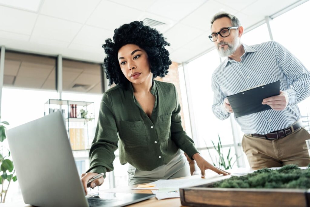 Executive assistant working on a laptop while an executive reviews notes beside her in a modern office